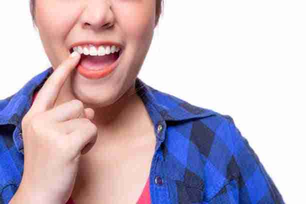 Cropped shot of a woman in blue checkered shirt, pointing to her healthy white teeth on a white background.